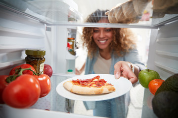 View Looking Out From Inside Of Refrigerator As Woman Opens Door For Leftover Takeaway Pizza Slice
