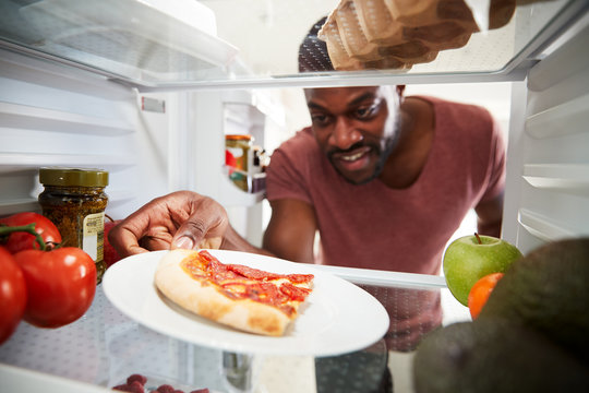 View Looking Out From Inside Of Refrigerator As Man Opens Door For Leftover Takeaway Pizza Slice