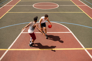 Young basketball player trying to defend ball from rival while carrying it
