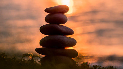 A pyramid of stones against the backdrop of the sea and the glare from the setting sun in the...