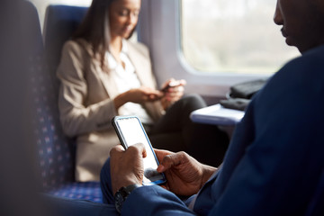 Close Up Of Business Passengers Sitting In Train Commuting To Work Looking At Mobile Phones