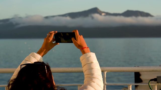 Young woman taking photos of fjord in northern Norway with phone from cruise ship