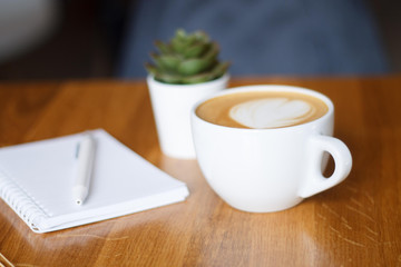 coffee in a Cup with a heart on a wooden table with a notebook and a tablet in a cafe with a flower work in the morning