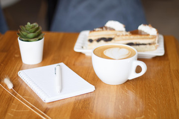 coffee in a Cup with a heart on a wooden table with a notebook and a tablet in a cafe with a flower work in the morning