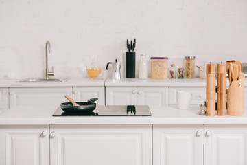 spacious kitchen with white furniture and frying pan on cooking surface