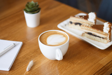 coffee in a Cup with a heart on a wooden table with a notebook and a tablet in a cafe with a flower work in the morning