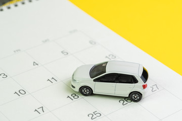 Car loan payment, buying new car or yearly maintenance schedule concept, miniature white car on clean calendar with date on yellow background