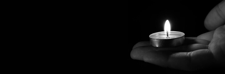 Candle in hand burning in the black background.