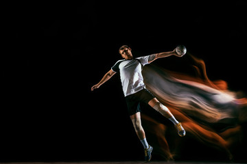 Fototapeta na wymiar Caucasian young handball player in action and motion in mixed lights over black studio background. Fit male professional sportsman. Concept of sport, movement, energy, dynamic, healthy lifestyle.