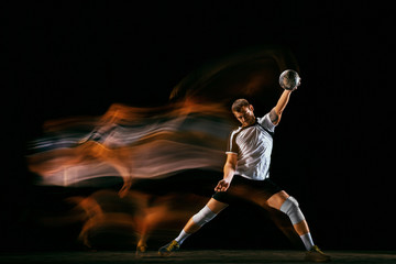 Caucasian young handball player in action and motion in mixed lights over black studio background....