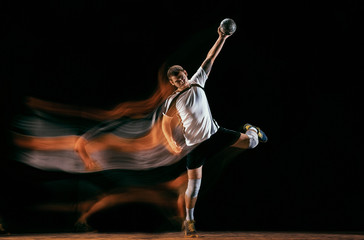 Caucasian young handball player in action and motion in mixed lights over black studio background....
