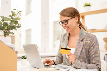 Young successful businesswoman with plastic card looking through online goods