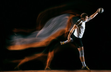 Caucasian young handball player in action and motion in mixed lights over black studio background....