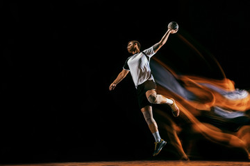 Caucasian young handball player in action and motion in mixed lights over black studio background....