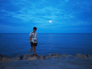 Asian man standing relaxedly alone on the road nearby the sunset beach.