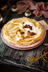 Homemade stack of thin crepes with sour cream and red jam on vintage pink plates