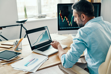 Rear view of man in smart casual wear analyzing stock market data while sitting in the office