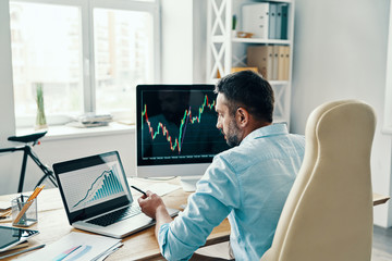 Rear view of man in smart casual wear analyzing stock market data while sitting in the office