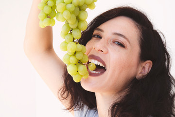 Smiling girl holding grapes near her face and smiling broadly to the viewer. Concept of home brew vine.