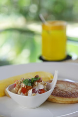 Breakfast served on the table, fruit salad with muesli, American pancake, omelet and  a glass of fresh orange juice