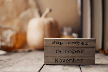 Wooden blocks against a rustic wood background with pumpkins and autumn leaves. Background with candle and pumpkin. Autumn background. Autumn months.