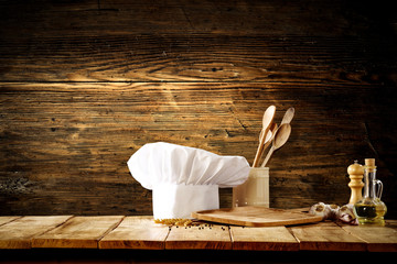 Fototapeta na wymiar White cook hat with kitchen tools on wooden background