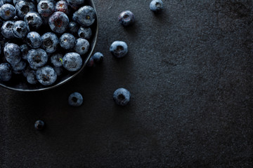 Fresh blueberries in a dark ceramic bowl on a black background, top view, close-up, copy space