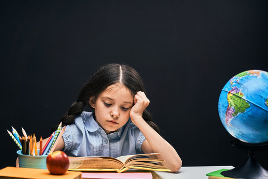 Back to school. concentrated handsome student reading a book sitting at the table. A child in the classroom with a Board in the background.