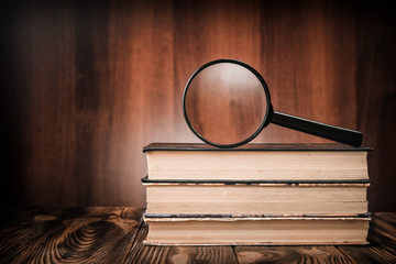 A magnifying glass on a stack of old books on a wooden table