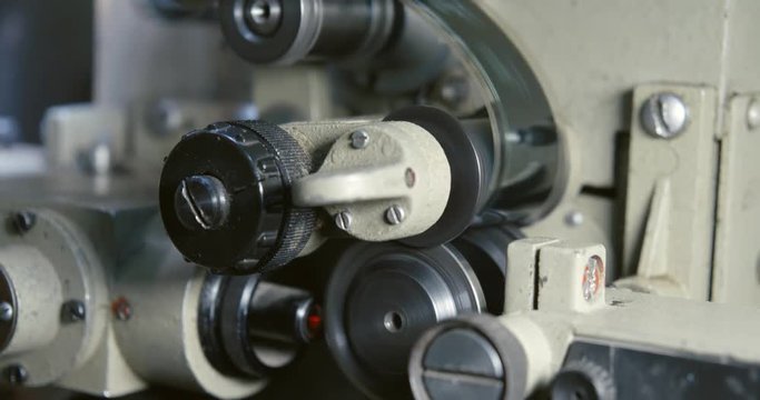 Close-up of a 35mm film in movie projector. Tape drive mechanism of cine-film in projector. Clamping guide rollers and gear drums.