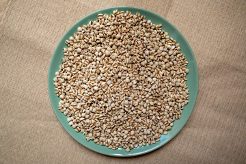 Picture of millet or job’s tears in a green dish that is grains and food on a brown tablecloth, wood grain, suitable for food advertising,top viwe