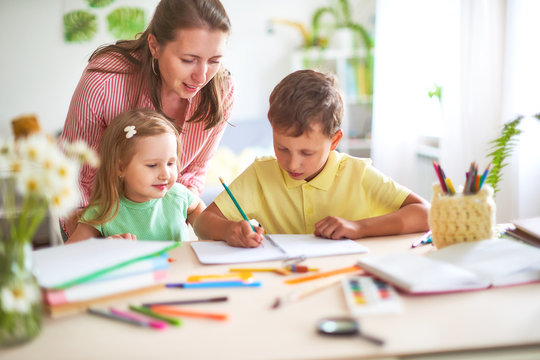 mother daughter and son draws pencil on a sheet of paper sitting at home at the table in a bright room.