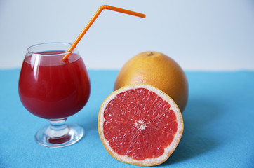 a glass of freshly squeezed red grapefruit juice and sliced ​​half a grapefruit and a grapefruit on a blue background. With copy space for text. Healthy food, diet concept, detox.