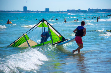 View of the seashore, resting people. In the foreground, a young man pulls a sail to the shore. Photographed from the back.