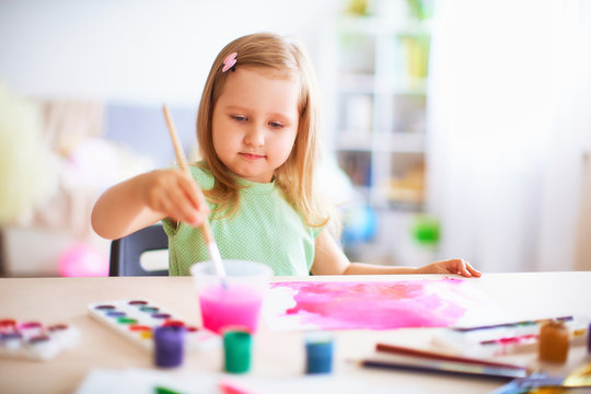 joyful girl child draws gouache in different colors on a white sheet of paper.