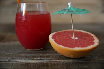 a glass of fresh red grapefruit juice with a straw and sliced ​​half a grapefruit with an umbrella on a rustic wooden background. Close-up. Healthy food, diet concept, detox