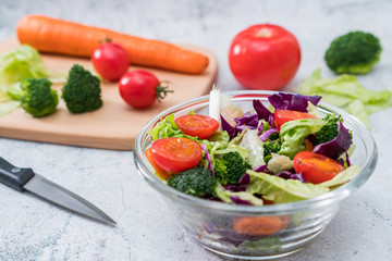 A bowl of vegetable salad and various vegetables on a cutting board