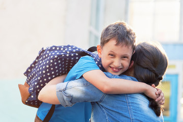 Back to school. Happy mother and son embrace in front of the elementary school.