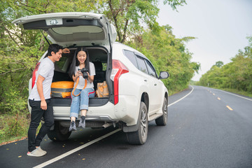Couple traveler with camera sitting on hatchback car with natural background . Young traveler  woman taking a photo and sitting on hatchback car .