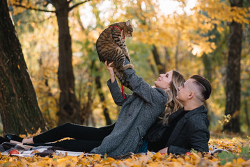 Beautiful young couple resting in autumn park. autumn concept. Loving couple resting with their cat.