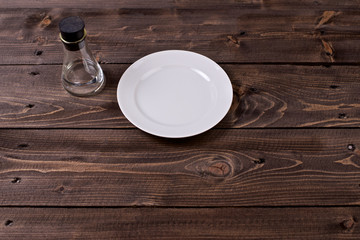 A clean white round plate and a beaker of clean water on wooden surface