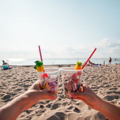 Hand holding cocktail with garbage on background of clean beach, ocean waves. Plastic ocean pollution, environmental crisis. Say no plastic. Single-use plastic waste