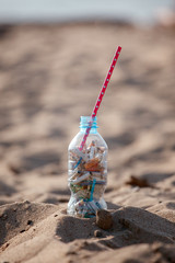 Cocktail with garbage and straw on clean beach. Plastic ocean pollution, environmental crisis. Say no plastic. Single-use plastic waste, world ocean day, eco concept