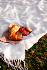 Croissants and fig peaches on a white plaid lie on the grass. Picnic on a sunny day.