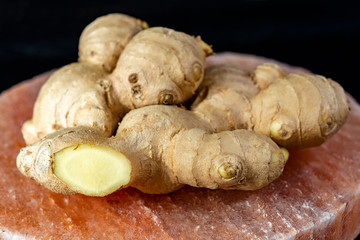 Fresh ginger roots on pink salt board close up on black wooden background