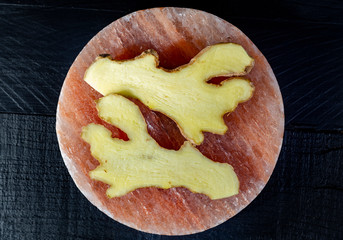 Fresh ginger roots on pink salt board close up on black wooden background