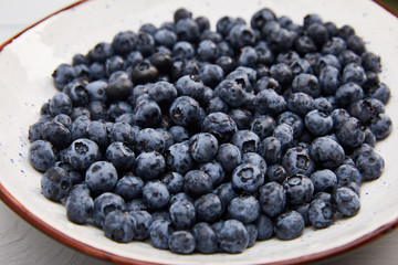 plate with delicious organic blueberries on white wooden table