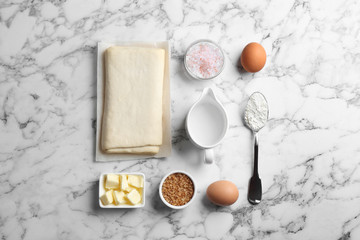 Flat lay composition of puff pastry dough and ingredients on white marble table