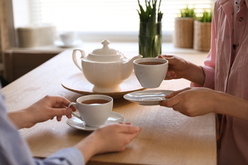 Women with cups of tea at table near window indoors, closeup - Powered by Adobe