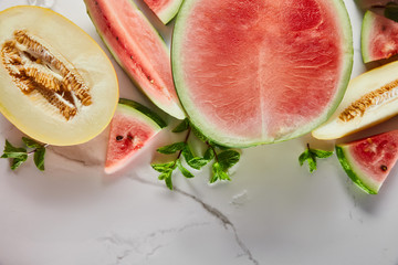 top view of cut delicious exotic red watermelon with melon and mint on marble surface